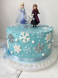 a frozen princess themed cake with two figurines on top and snowflakes