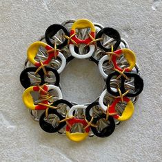 a multicolored bracelet is hanging on a white wall with black, yellow and red circles