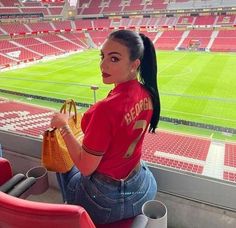 a woman sitting in the stands at a soccer stadium holding a handbag and purse