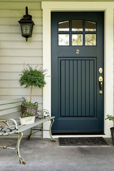 the front door is painted blue and has potted plants on the bench in front