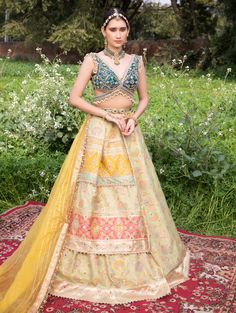 This exquisite pure silk banarasi lehenga features a mirror-embellished, asymmetrically draped double layer in soft peach, adorned with handcrafted zardozi embroidery and resham work. Paired with a heavily embroidered deep-neck cutout blouse embellished with pearl latkans, the ensemble exudes elegance. The look is completed with a shimmering gota patti textured organza dupatta, also adorned with pearl latkans, and our signature meenakari kamarband with latkans, creating a stunning blend of tradition and modernity. Elegant Semi-stitched Pista Green Lehenga, Semi-stitched Yellow Lehenga With Dabka Details, Embellished Pista Green Georgette Lehenga, Fitted Pista Green Embroidered Lehenga, Pista Green Embellished Semi-stitched Lehenga, Cutout Blouse, Zardozi Embroidery, Silk Lehenga, Organza Dupatta