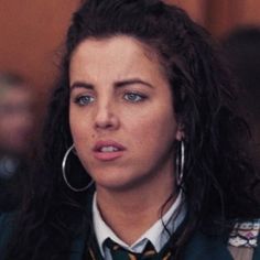 a woman with long hair wearing a green jacket and gold hoop earrings is looking at the camera