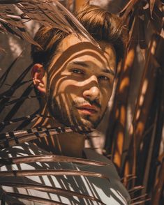 a man with sun painted on his face standing in front of some palm leaves and looking at the camera