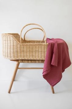 a wicker baby crib with a red blanket on it and a wooden chair