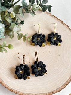 This listing is for one pair of black flower dangle earrings. Each flower is sculpted from black polymer clay. The petals were individually cut out and shaped into a flower shape with a textured heart on the back of the earring. Brass leaves were placed between the layers of petals and gold glitter was added to the flower centers. Please be advised that some glitter may fall off. Each earring was cured in the oven and the stud portion is nickel-free.  Care: Please treat your new earrings as litt Black Flower Charm Jewelry, Black Dangle Flower Earrings With Ear Wire, Adjustable Black Jewelry With Flower Charm, Adjustable Black Flower Earrings, Adjustable Black Flower Earrings For Pierced Ears, Black Jewelry With Flower Charm As Gift, Elegant Black Dangle Flower Earrings, Handmade Black Polymer Clay Earrings, Black Flower Earrings For Gift