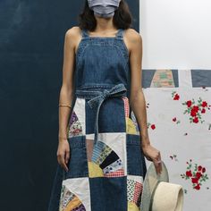 a woman with a mask on her face standing in front of a quilted wall