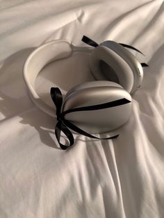 two white headphones laying on top of a white sheet covered bed with black ribbon