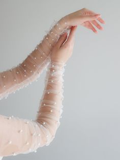 a woman wearing white gloves and holding her arm with pearls on the sleeves, in front of a gray background