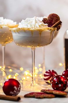 two glasses filled with white wine and topped with whipped cream next to christmas baubies