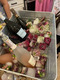 two bottles of wine and ice cubes in a container on a counter top next to a woman