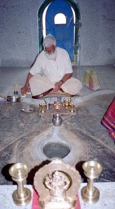 a man sitting on the ground in front of a toilet with candles around it and an open door behind him