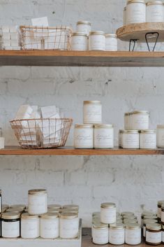 shelves with jars and baskets on them in front of a white brick wall that is filled with other items