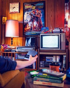 a man sitting in front of a tv holding a remote control and pointing at it