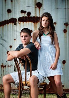 a young man and woman sitting on a chair in front of a rusted building