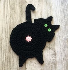 a crocheted black cat with green eyes laying on top of a wooden floor