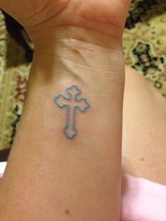 a woman's wrist with a small blue cross tattoo on her left side arm