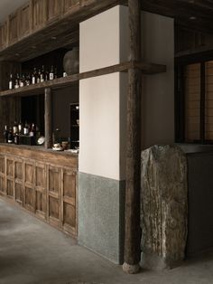 an empty bar with wooden shelves and bottles on the back wall, next to a stone block