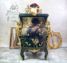 an ornate painted chest of drawers next to a vase with flowers on it and a gold frame