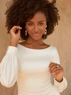 a woman in a white dress is posing for a photo with her hand on her head