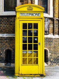 a yellow telephone booth sitting in front of a brick building