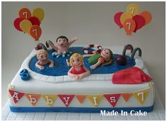 there is a cake with people in the pool on it and balloons floating above them