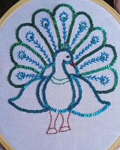 a white peacock with green and blue beads on it's tail is sitting in front of an embroidery hoop