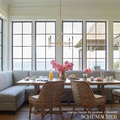 a dining room table with two chairs and a bench in front of large windows overlooking the water