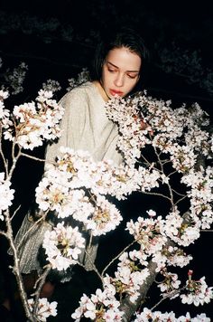 a woman standing in front of a tree with white flowers on it's branches