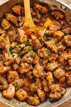 a pan filled with meat and vegetables on top of a wooden table next to a spoon