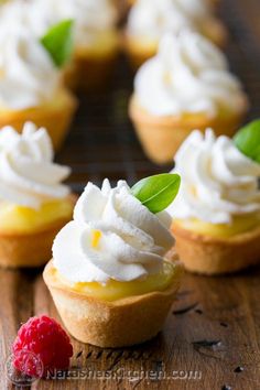 small cupcakes with whipped cream and raspberries on a wooden table top