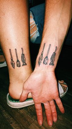 two people with matching tattoos on their arms holding hands and brooms in the other hand