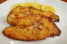 two pieces of chicken on a plate with lemon wedges