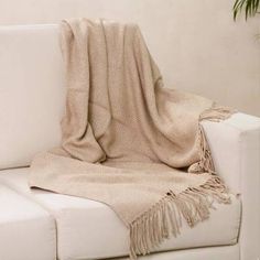 a white couch with a tan blanket on it and a potted plant in the corner