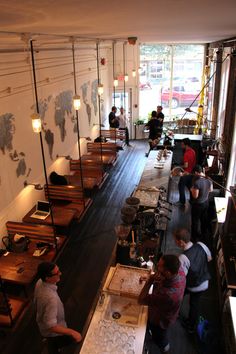 several people are standing in a room with tables and stools on the floor, looking down at them