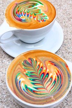 two coffee cups with designs on them sitting next to each other in white saucers