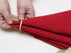 someone cutting fabric with scissors on top of red napkins that are folded in half