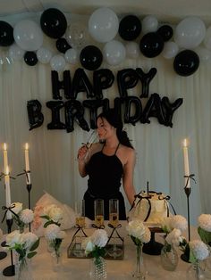 a woman standing in front of a table filled with white and black balloons, candles and flowers