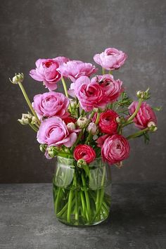 a vase filled with pink and red flowers on top of a table next to a gray wall