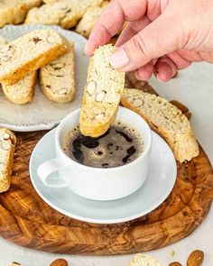 someone dipping something into a cup of coffee with almonds around it on a wooden board