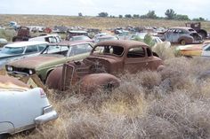 an old rusted out car sits in the middle of a field full of junk