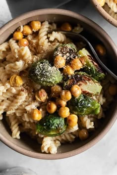 two bowls filled with pasta, broccoli and chickpeas on a table