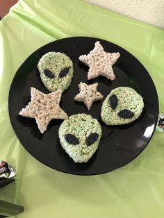 some cookies are on a black plate with green and white frosting, stars and eyes