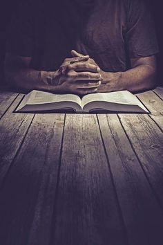 a man sitting at a table with his hands folded over an open book in front of him