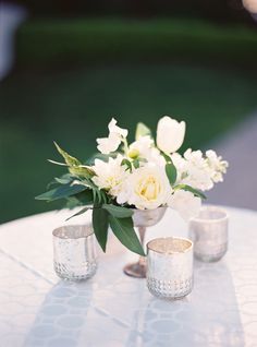 white flowers and greenery in silver vases on a round table with two candles