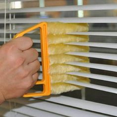 a person is cleaning the blinds with a yellow duster and cloth on top of it