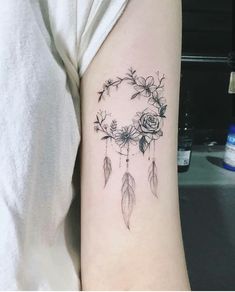 a woman's arm with a tattoo that has flowers and feathers on the side