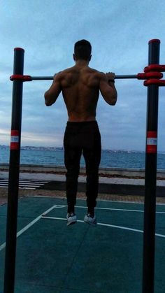 a man is doing pull ups on a bar in front of the ocean with his back to the camera