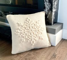 a white crocheted pillow sitting on top of a hard wood floor next to a fireplace