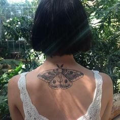 the back of a woman's neck with a moth tattoo on it