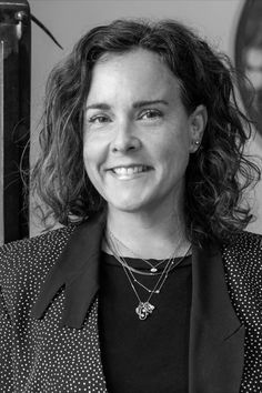 a black and white photo of a woman with curly hair wearing a suit smiling at the camera